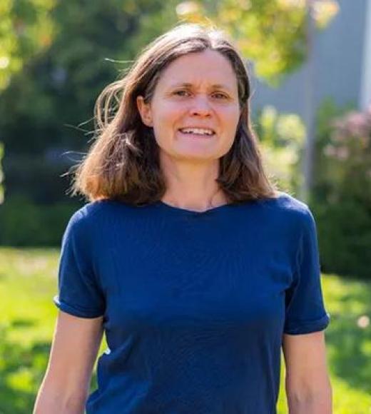 Outdoor portrait of a smiling woman in a blue shirt standing in a sunlit garden