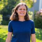 Outdoor portrait of a smiling woman in a blue shirt standing in a sunlit garden